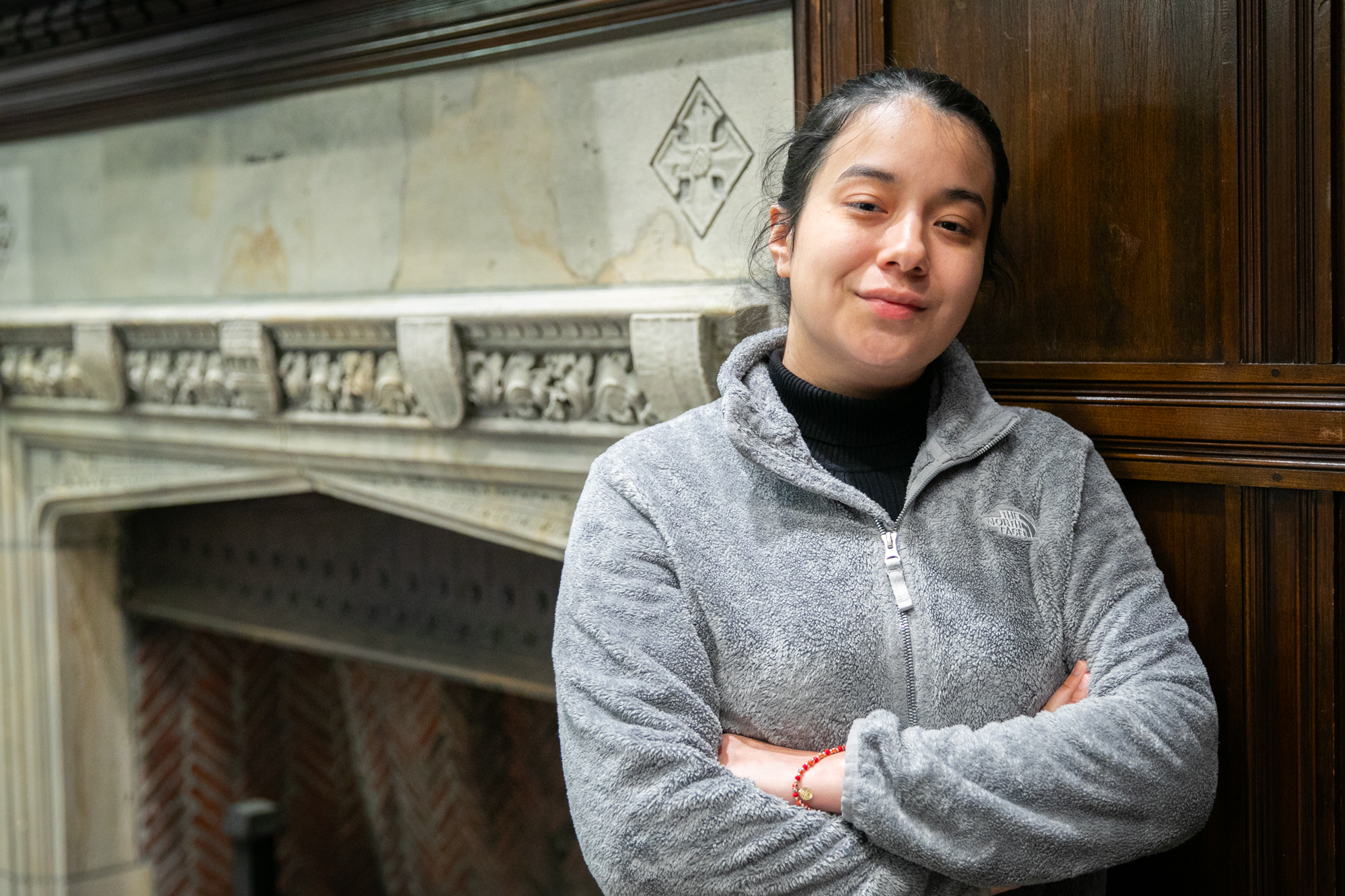 Penn fourth-year Daisy Arizmendi poses near a stone fireplace inside a sitting room at The ARCH building on Penn's campus.